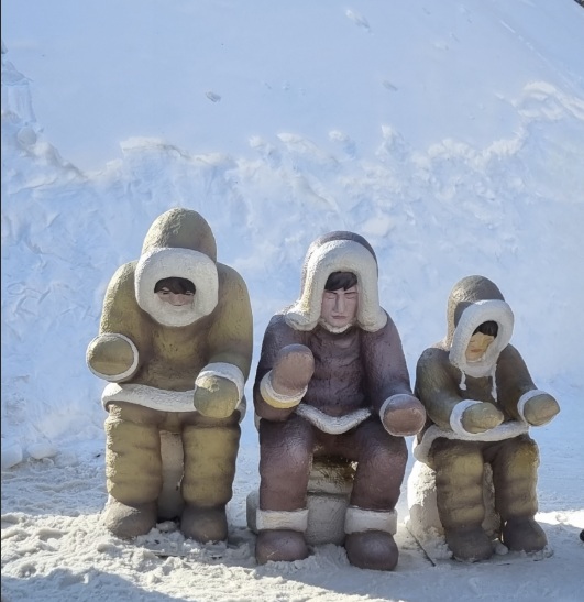 Snow sculptures depicting people in winter clothing at a Gangwon winter festival, carved from packed snow against a snowy outdoor backdrop