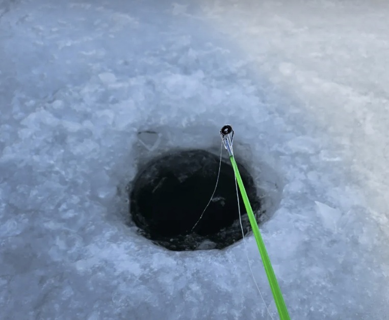 Ice fishing hole drilled into a frozen river in Gangwon Province, with fishing gear positioned above the ice