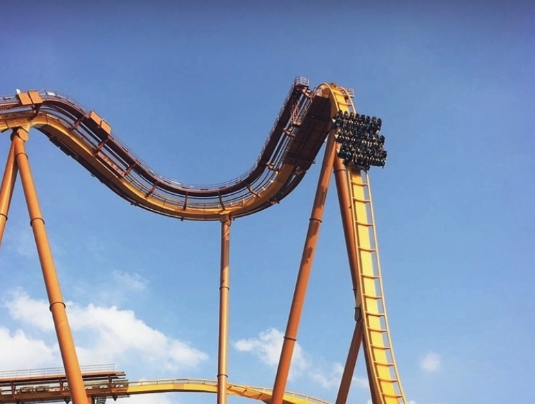 Dive coaster train hanging at the edge of a steep drop before its 90-degree vertical dive.