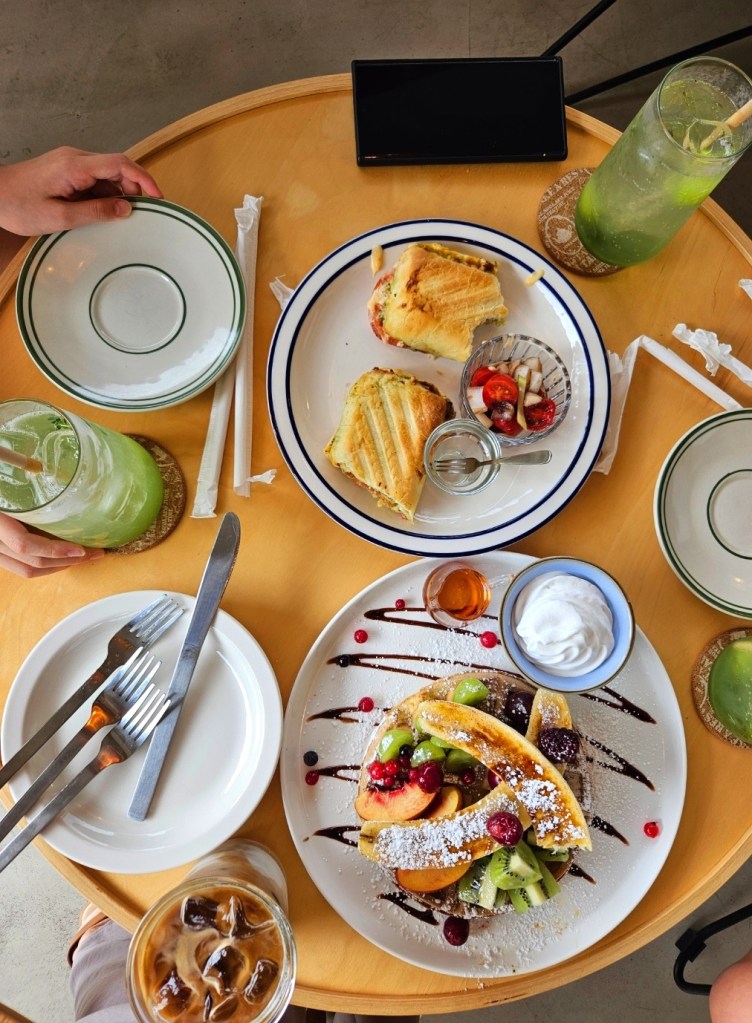 Brunch at Ô Mignon Café near Bulguksa Temple – fresh fruit waffles, panini sandwich, iced latte, and lime smoothies served on a round wooden table in Gyeongju.