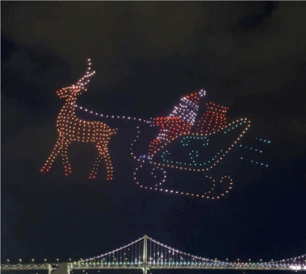 Santa and a reindeer formed by colorful drones during the Gwangalli Drone Show in Busan, with Gwangan Bridge glowing in the background.