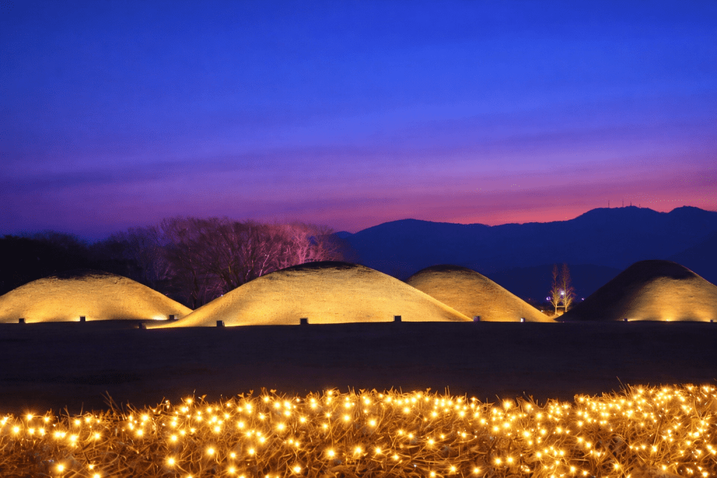 Evening view of ancient burial mounds in Gyeongju illuminated at dusk, creating a calm and atmospheric scene for a family night walk