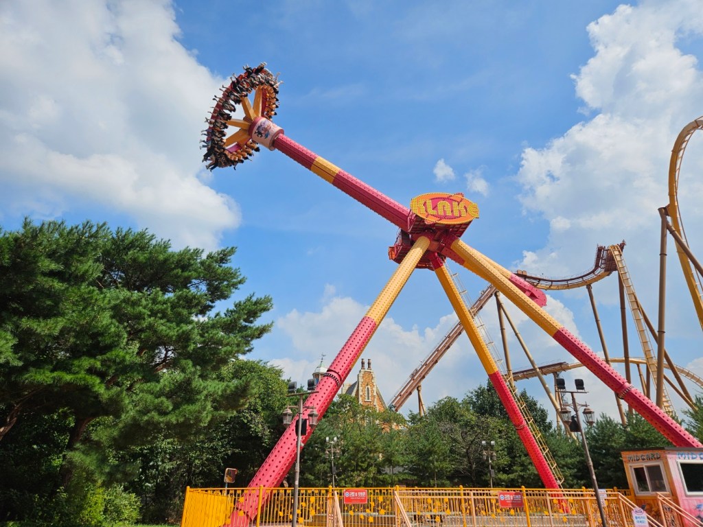Large pendulum thrill ride swinging high into the sky with riders seated in a circular platform.
