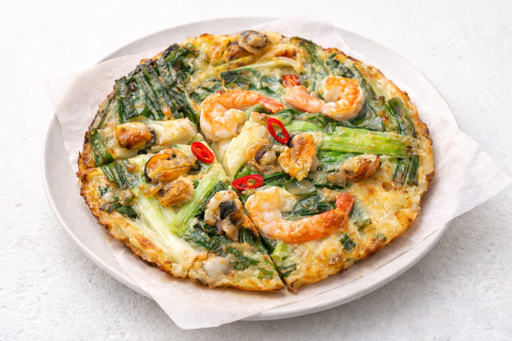 Korean haemul pajeon seafood pancake with shrimp, squid, green onions, and chili peppers served on a white plate