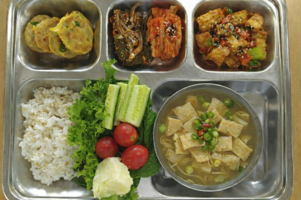 Balanced South Korean public school lunch tray with rice, side dishes, tofu tangsuyuk, and fish cake soup